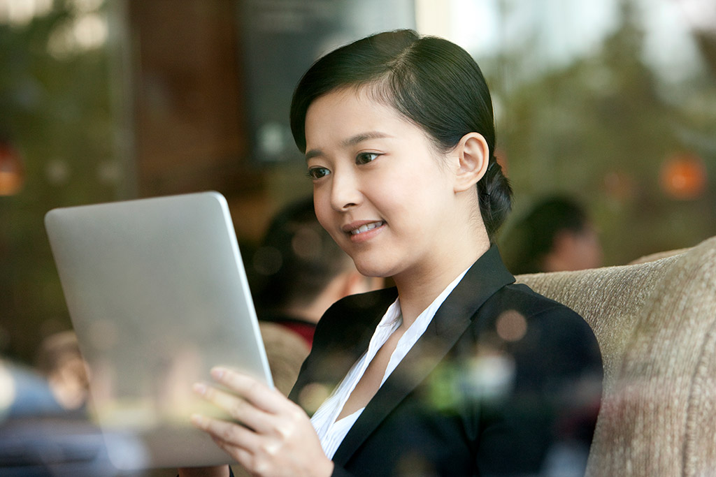 Cheerful Chinese businesswoman playing digital tablet in cafe